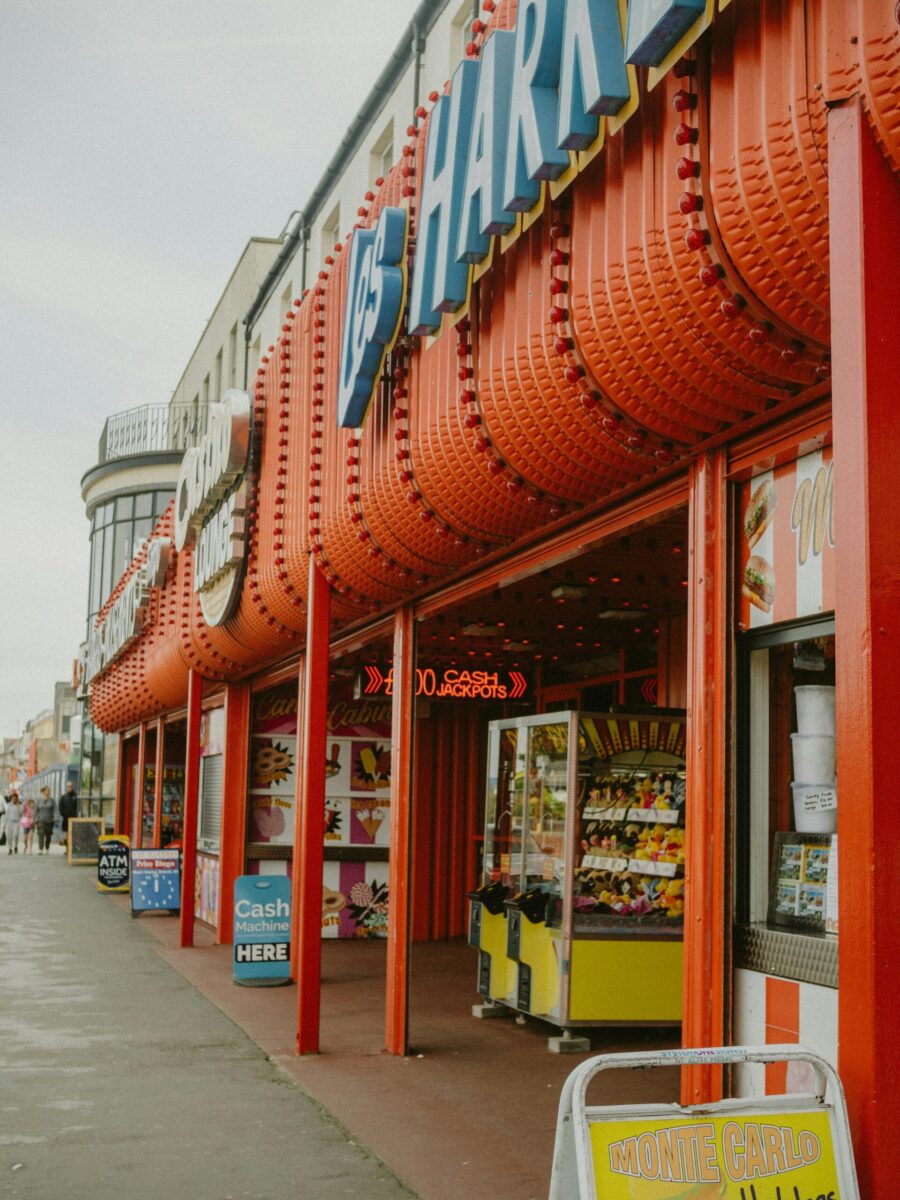 Colorful carnival arcade entrance with neon signage on an overcast day, attracting visitors on the sidewalk.